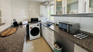 A compact kitchen with a washing machine, microwave, and a sink.