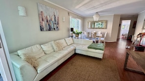 A living room with a sectional sofa, a chandelier, a dining area with chairs, and a large window.