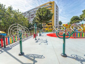 Ein Spielplatz mit Sportgeräten, einer Radrennbahn und einem gelben Gebäude im Hintergrund.