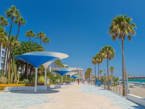 A promenade with palm trees, blue umbrellas, and a beach in the background. - Neptuno Apartment in Estepona, 3 bedrooms, air conditioning (Estepona)