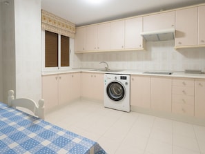 A compact kitchen with a washing machine, a sink, and a window with blinds. - Neptuno Apartment in Estepona, 3 bedrooms, air conditioning (Estepona)