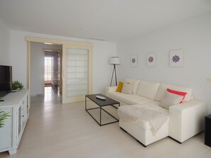 Ein modernes Wohnzimmer mit einem weißen Sofa, einem Couchtisch, einem Fernseher und einer Stehlampe.