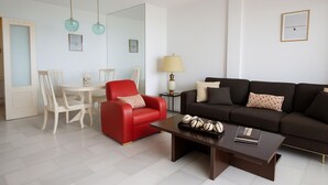 Una sala de estar moderna con un sillón rojo, un sofá marrón oscuro, una mesa de centro y un comedor con una mesa y sillas.