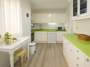 A compact kitchen with white cabinets, a green countertop, a sink, a microwave, and a small dining area with a table and chair. - Apartment with Parking in Estepona, by the Sea (Estepona)