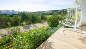 Een balkon met een witte stoel, uitzicht op een groen landschap en gebouwen op de achtergrond.