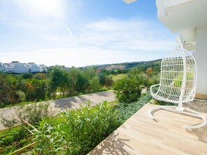 A balcony with a white chair, a view of a green landscape, and buildings in the background. - Luxury Apartment in Estepona with Terrace and Parking (Estepona)