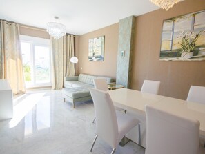 A modern living room with a dining area, a large window, and a chandelier. - Luxury Apartment in Estepona with Terrace and Parking (Estepona)
