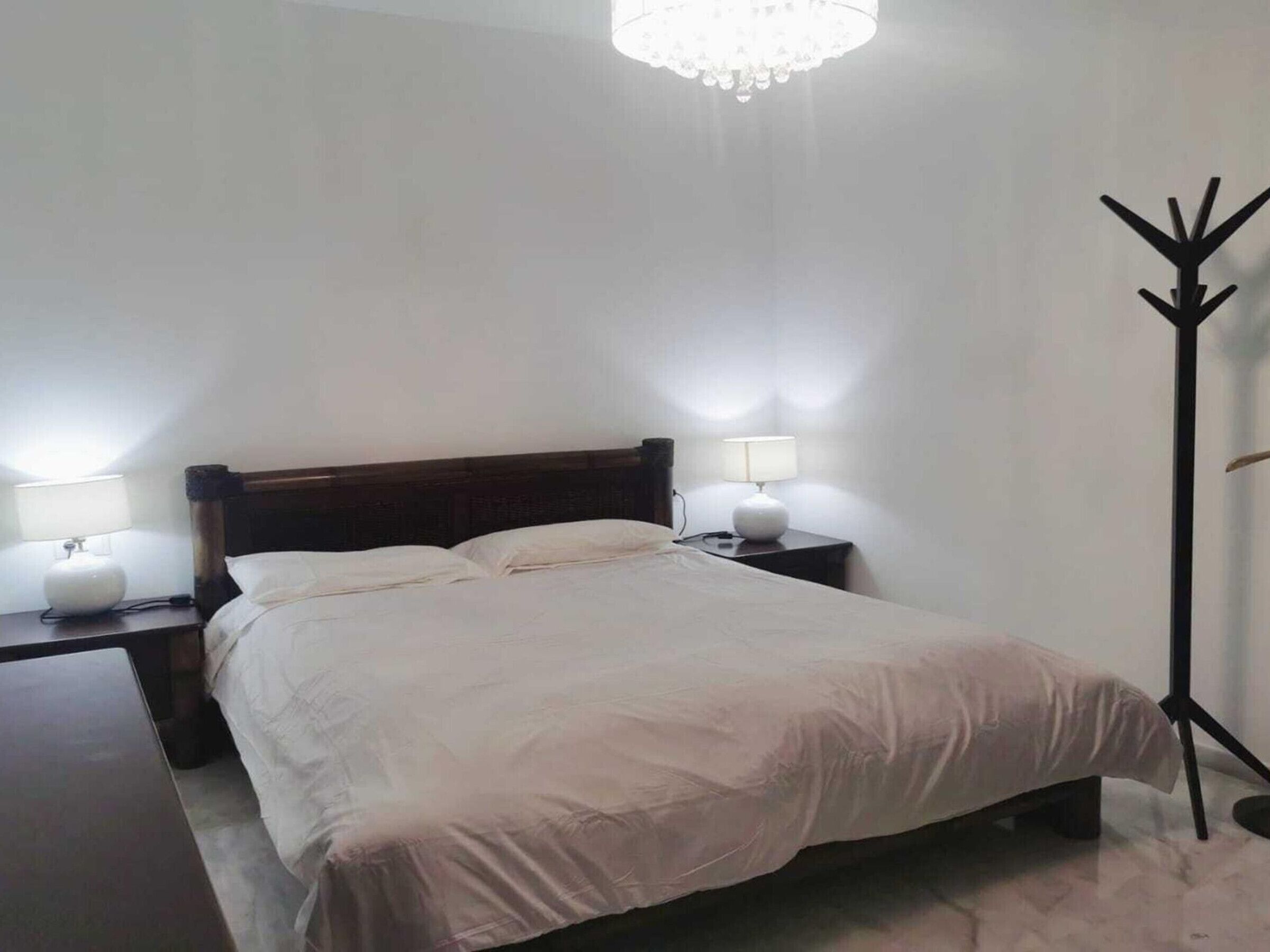 A bedroom with a bed, two bedside tables with lamps, a floor lamp, and a chandelier.