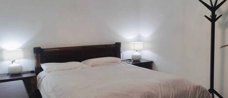 A bedroom with a bed, two bedside tables with lamps, a floor lamp, and a chandelier.