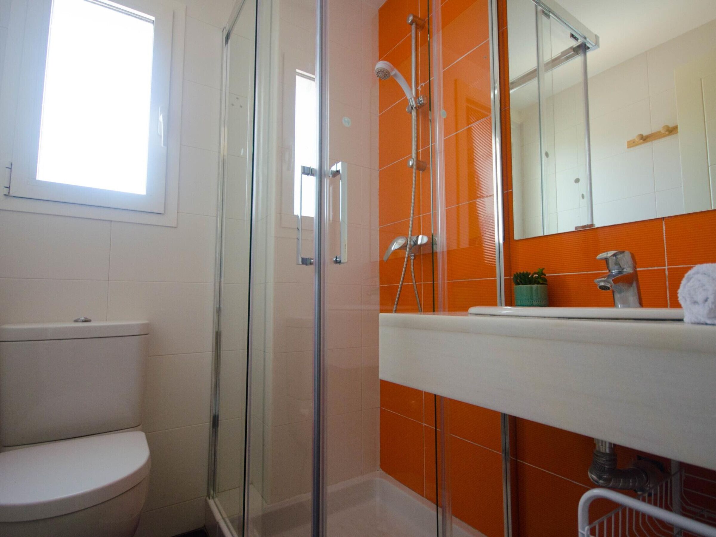 Une salle de bain avec une douche à parois de verre, des toilettes blanches et un lavabo dont le plan est recouvert de carreaux orange.