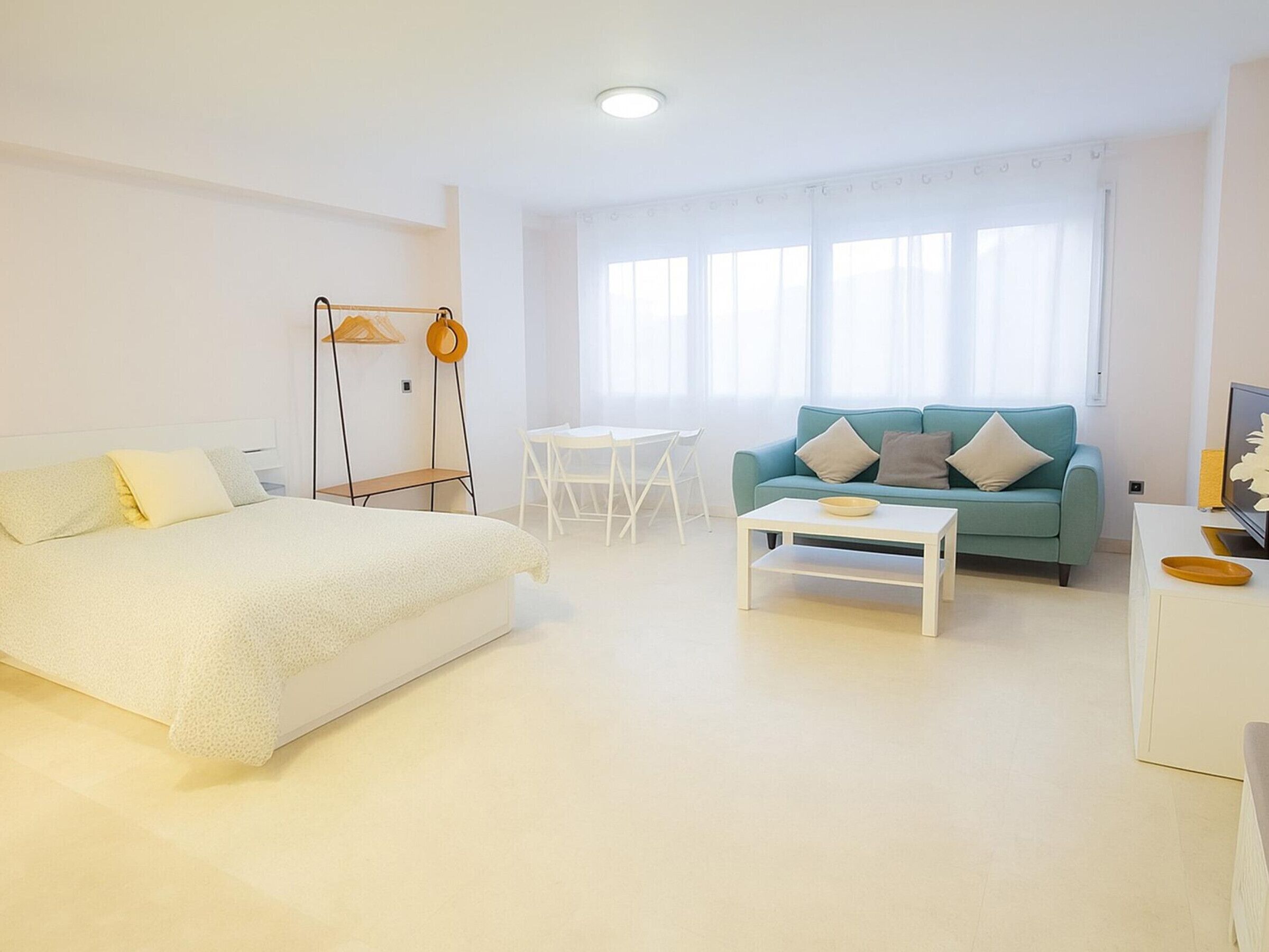 Una habitación minimalista con cama, sofá, mesa de centro y mueble para televisión.