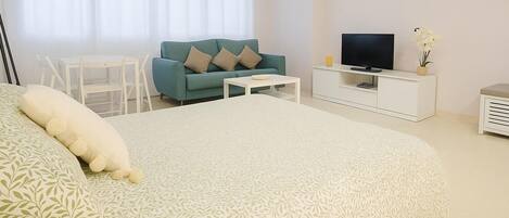 Un dormitorio con una cama grande, televisor, sofá y una mesita.