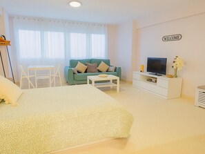 Habitació moderna amb llit, sofà, televisió, armari blanc i un rètol que diu 'WELCOME'.