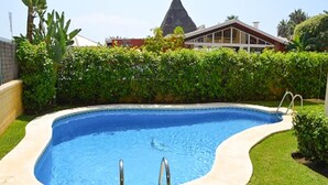 Ein Schwimmbecken mit geschwungener Kante, umgeben von einem gepflegten Rasen und einer Hecke.