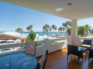 En balkon med udsigt over stranden, palmer og en bygning, der hedder 'Lisoicion ABARDERO'.