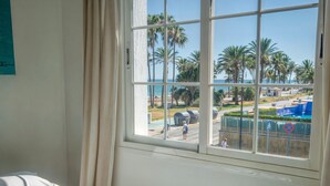 Ein Hotelzimmer mit großem Fenster, einem Bett mit blumigem Überwurf und Blick auf einen Resortbereich mit Palmen und einem Pool.