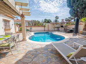 Una piscina con baldosas de piedra, sillas de descanso, una mesa y una pérgola.