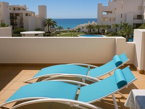 Eine Dachterrasse mit blauen Lounge-Stühlen und Blick auf das Meer.