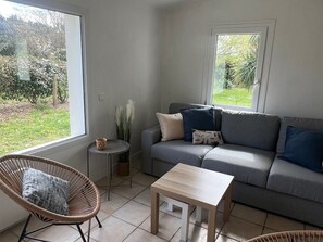 A living room with a grey sofa, a wooden coffee table, a wicker chair, and a small side table with a vase. - Cozy house, pets welcome - 6 guests (Bangor)