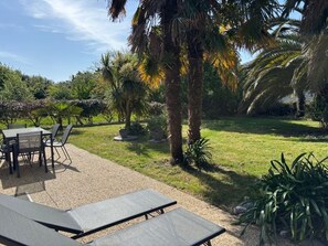 An outdoor patio area with a table and chairs, surrounded by palm trees and greenery. - Cozy house, pets welcome - 6 guests (Bangor)