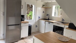 A modern kitchen with a stainless steel refrigerator, white cabinets, a wooden countertop, and a window with a view of greenery.