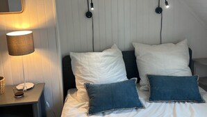 A bedroom with a bed, two wall-mounted lamps, a framed fish picture, a bedside table with a lamp, and a mirror.