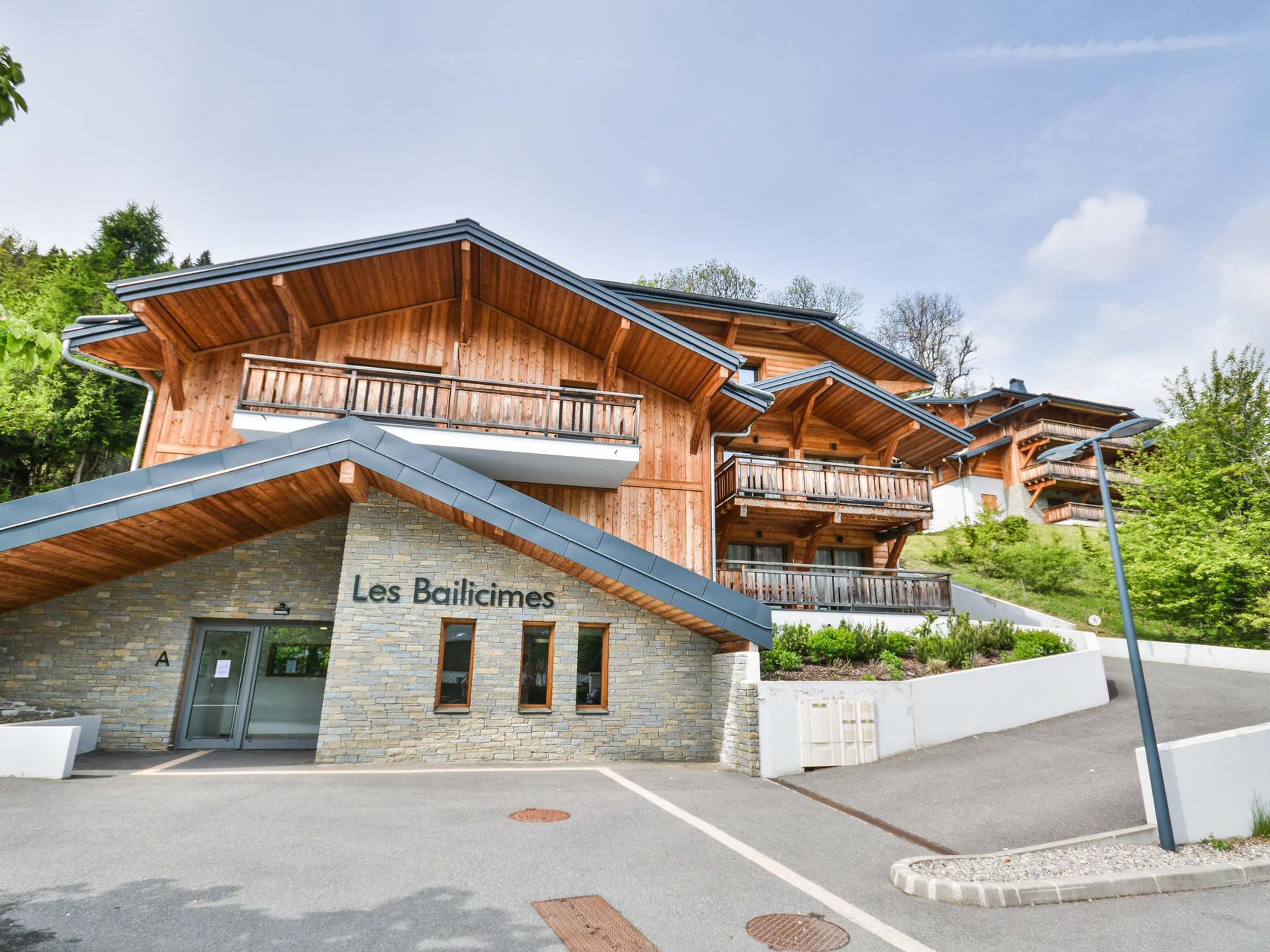 Un bâtiment en bois doté de balcons et d’une façade en pierre, portant l’inscription « Les Bailicimes ».