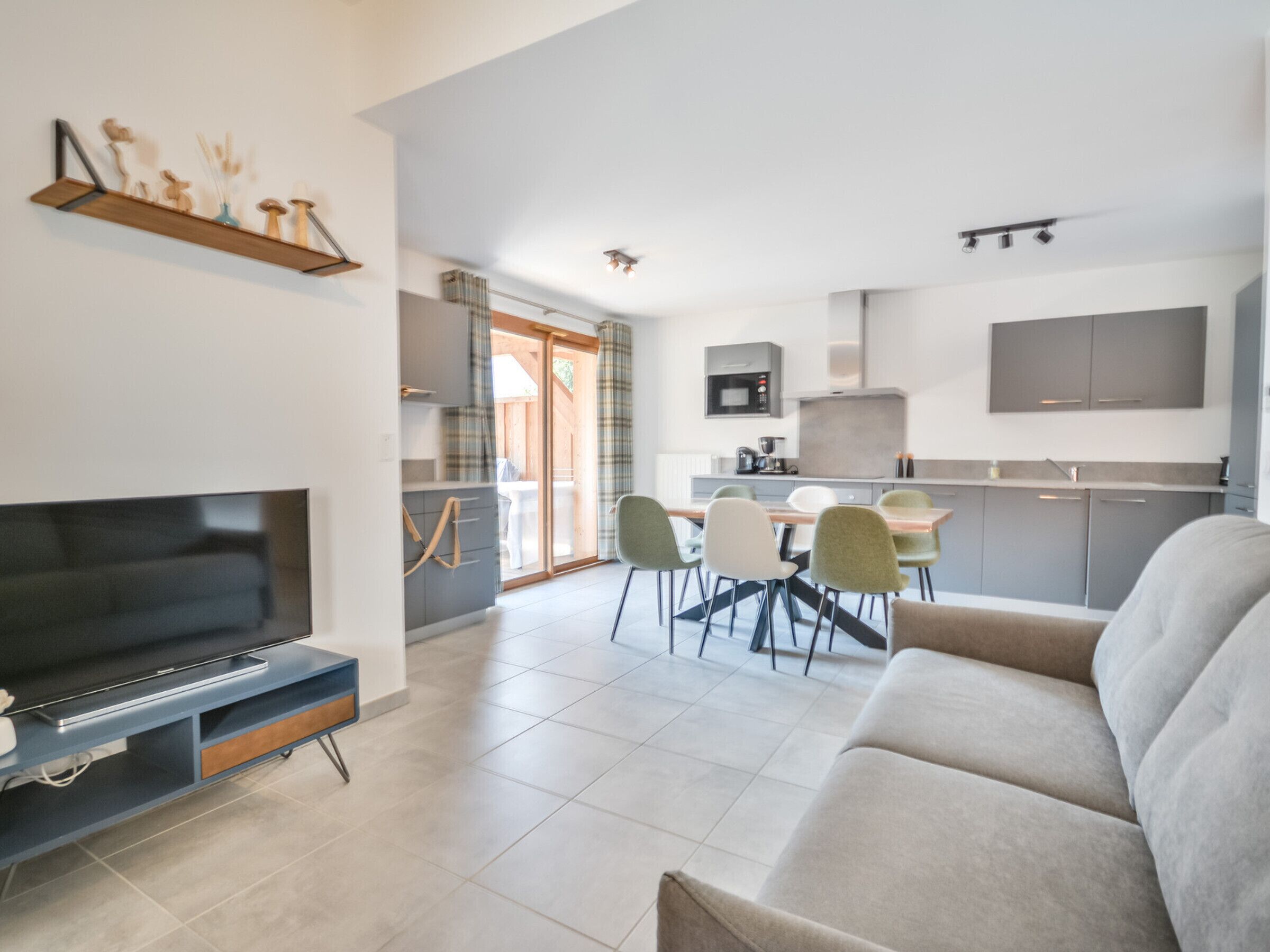 A modern living room with a flat-screen TV, a sofa, and a dining area with chairs and a table.