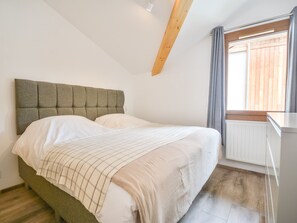 Ein Schlafzimmer mit Bett, einem Fenster mit Vorhängen, einem Heizkörper und einem Holzbalken an der Decke.