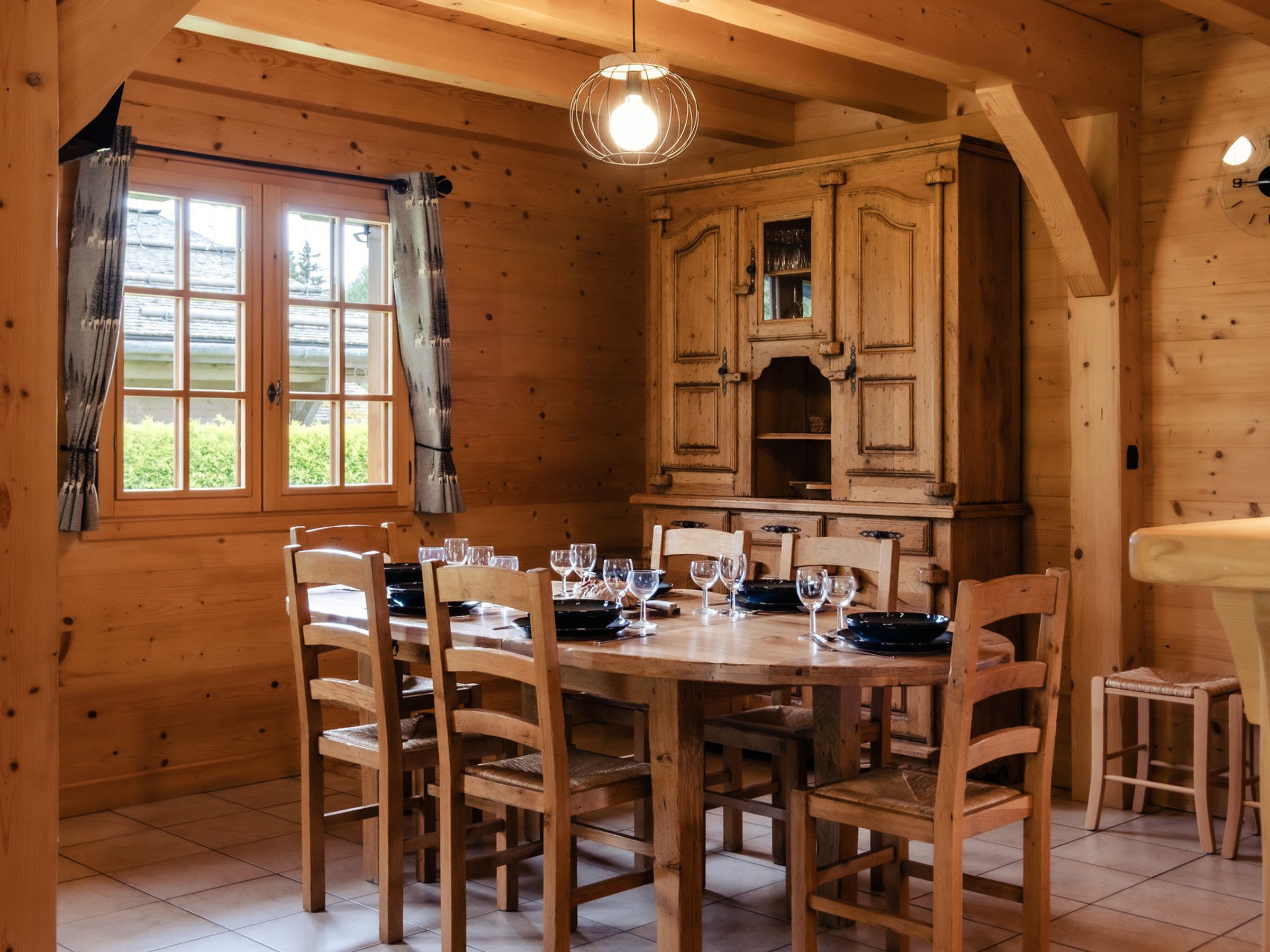 Un intérieur en bois avec une table à manger dressée pour quatre personnes, entourée de chaises.