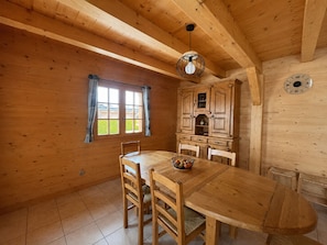 Un interior de madera con una mesa de comedor, sillas, una lámpara colgante, una ventana con cortinas y un reloj en la pared.