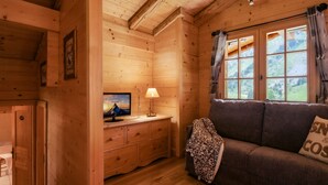 Ein gemütliches Holzblockhaus-Interieur mit einer Couch, einem Fernseher auf einer Holzkommode und einem Fenster mit Vorhängen.