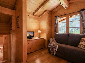 A cozy wooden cabin interior with a sofa, a television on a wooden dresser, and a window with curtains. - 4★ chalet, pets allowed, 9 guests, panoramic view (La Clusaz)