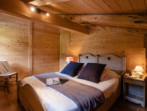 Ein Schlafzimmer einer Holzhütte mit Bett, Nachttisch, Stuhl und Deckenleuchte.