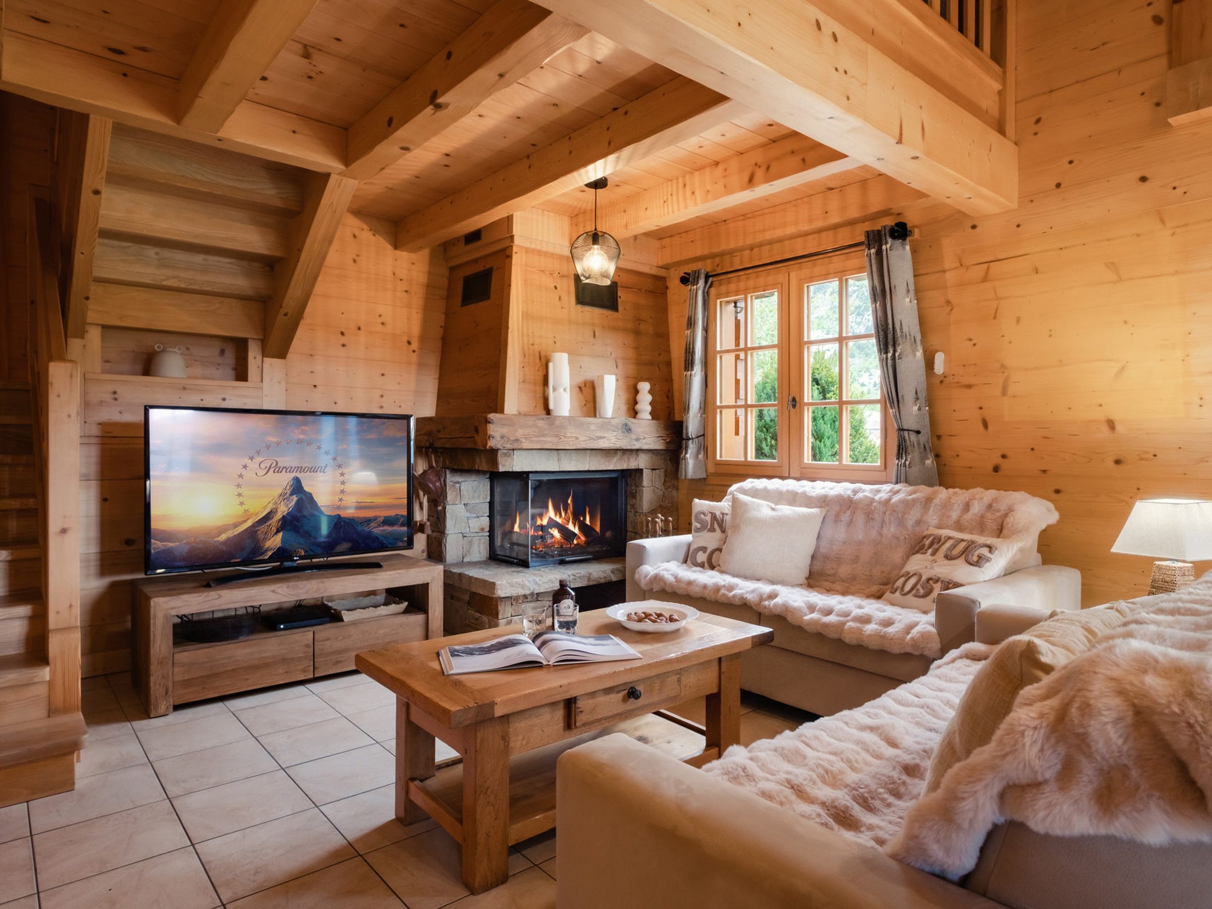 A cozy log cabin interior with a fireplace, a television, a sofa, and a dining table.