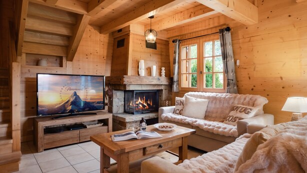 Ein gemütliches Blockhaus-Interieur mit Kamin, Fernseher, Sofa und Esstisch.