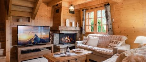 A cozy log cabin interior with a fireplace, a television, a sofa, and a dining table.
