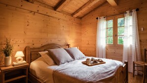 Ein Schlafzimmer einer Holzhütte mit Bett, Nachttisch, Lampe und einem Fenster mit Vorhängen.