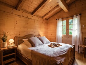 A wooden cabin bedroom with a bed, bedside table, lamp, and a window with curtains. - 4★ chalet, pets allowed, 9 guests, panoramic view (La Clusaz)