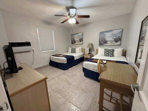 Ein Hotelzimmer mit zwei Betten, einem Schreibtisch, einem Deckenventilator und Bildern an den Wänden.