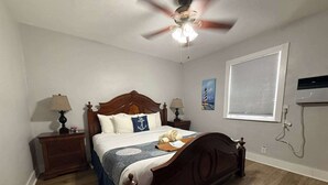 Ein Schlafzimmer mit einem hölzernen Bett, zwei Nachttischen mit Lampen, einem Deckenventilator, einem Fenster mit Jalousien und einem Bild an der Wand.
