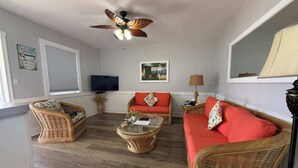 Ein Wohnzimmer mit Rattanmöbeln, einem Deckenventilator, einem Fernseher und einem Fenster mit Jalousien.