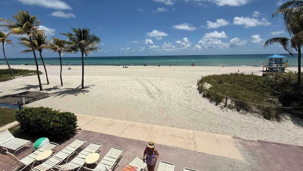 Ein Strand mit Liegestühlen, Palmen und einem Rettungsturm.