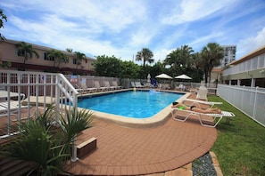 A swimming pool with lounge chairs, a fenced area, and a building in the background. - Oceanfront Retreat in Hollywood Beach (Hollywood)