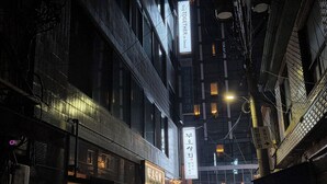 Una estrecha calle urbana nocturna con señalización e iluminación en edificios.