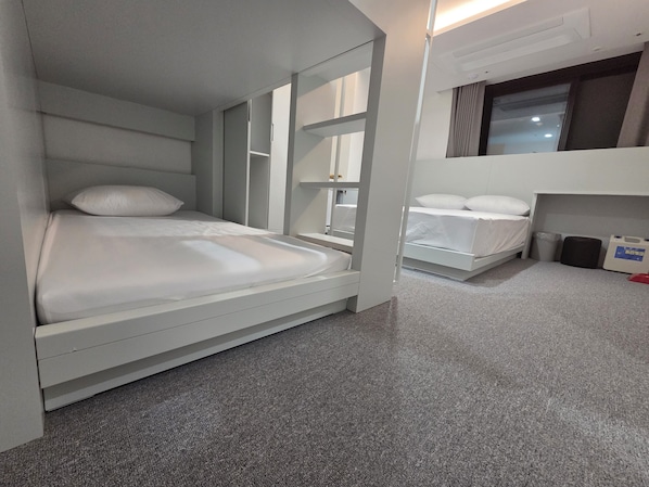 Une chambre d’hôtel moderne avec un lit superposé, un petit bureau, une chaise, une fenêtre et une poubelle.