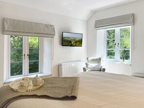 A bedroom with a bed, a chair, a radiator, and two windows with curtains. - Glen Cottage, Porlock (Porlock)