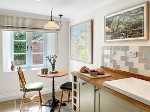 A kitchen with a wooden countertop, a dining table with chairs, a hanging light fixture, and a window with a view of greenery. - Glen Cottage, Porlock (Porlock)