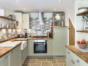 A compact kitchen with a built-in oven, a microwave, and a hanging pot rack. - Glen Cottage, Porlock (Porlock)