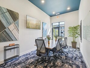 A conference room with a large table, four chairs, a potted plant, and artwork on the walls.